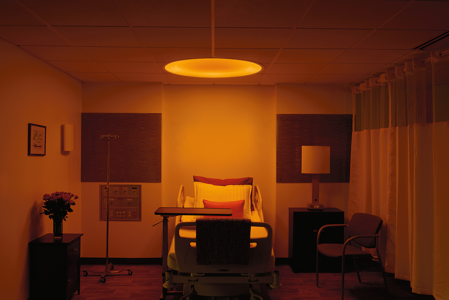 Symmetry patient room lighting fixture, a large, round overbed luminaire, in its amber night light mode.