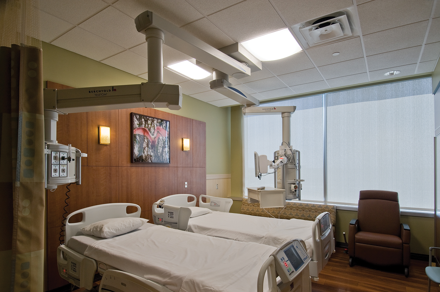 Unity medical lighting over two patient beds in a wood-paneled patient area.