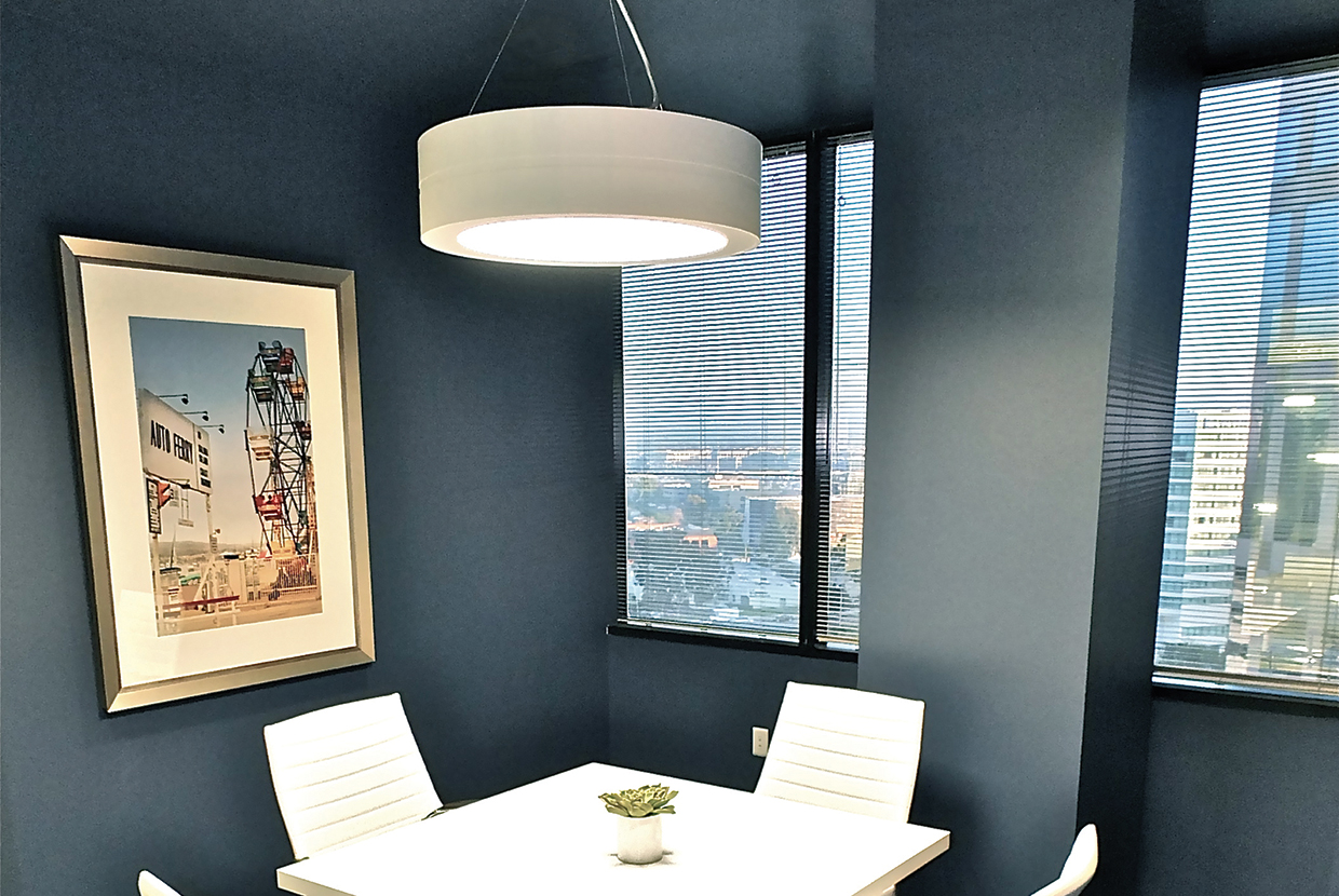 An Omnience pendant in an office lighting application above a small meeting table in a blue-carpeted meeting room.