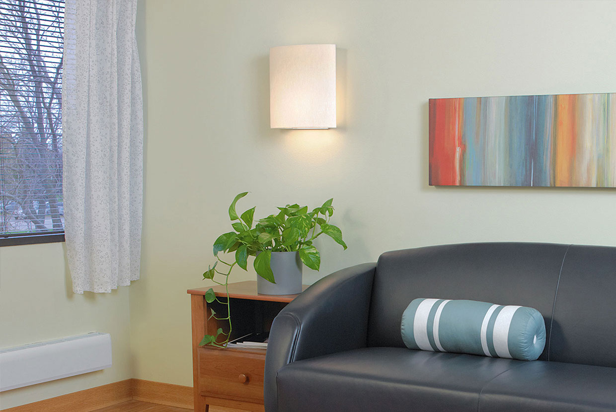 Unity wall sconce provides warm, inviting light in a hospitality lighting design near a sofa and side table. 