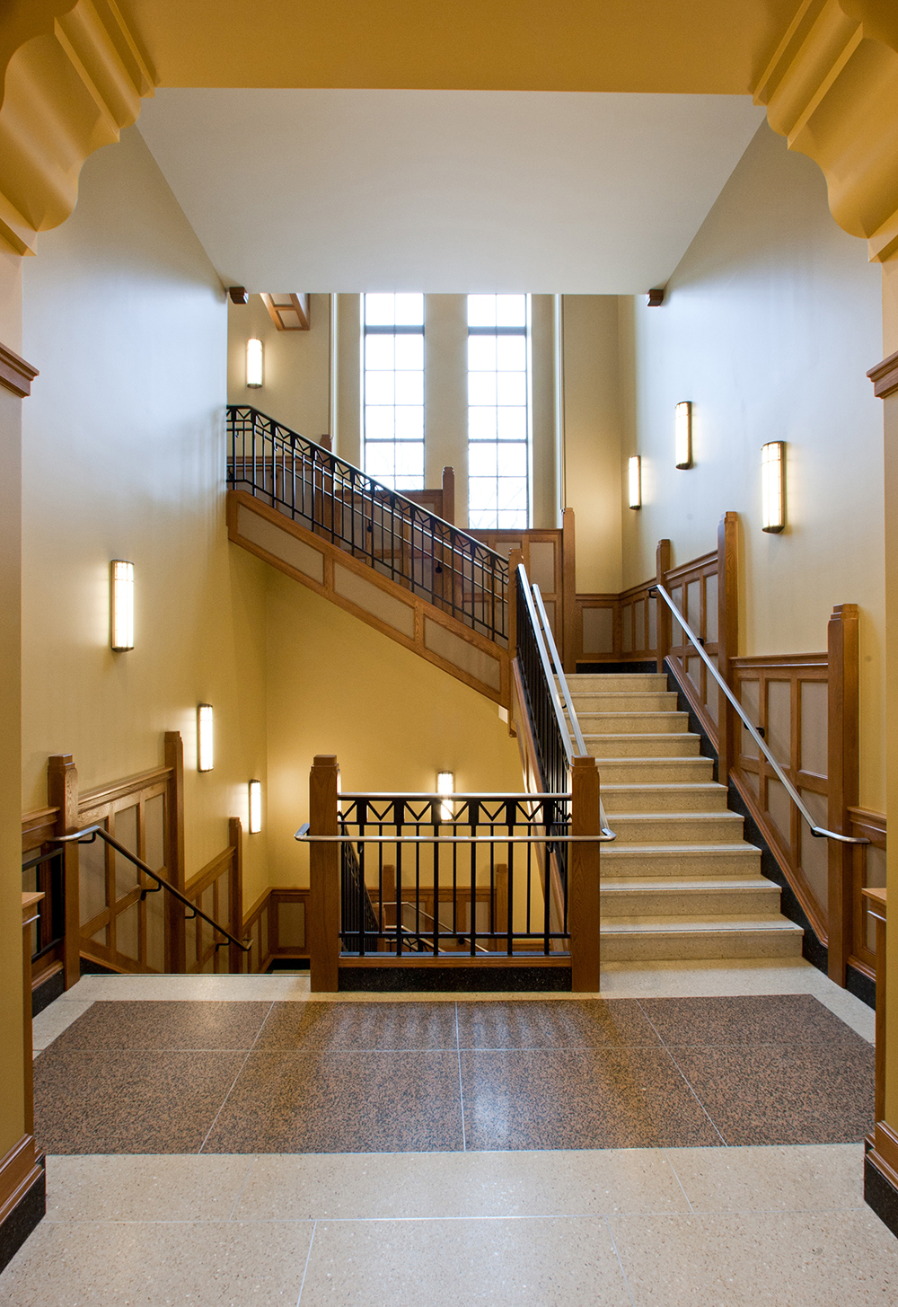 These wall-mounted custom light fixtures illuminate a traditional campus stairwell.