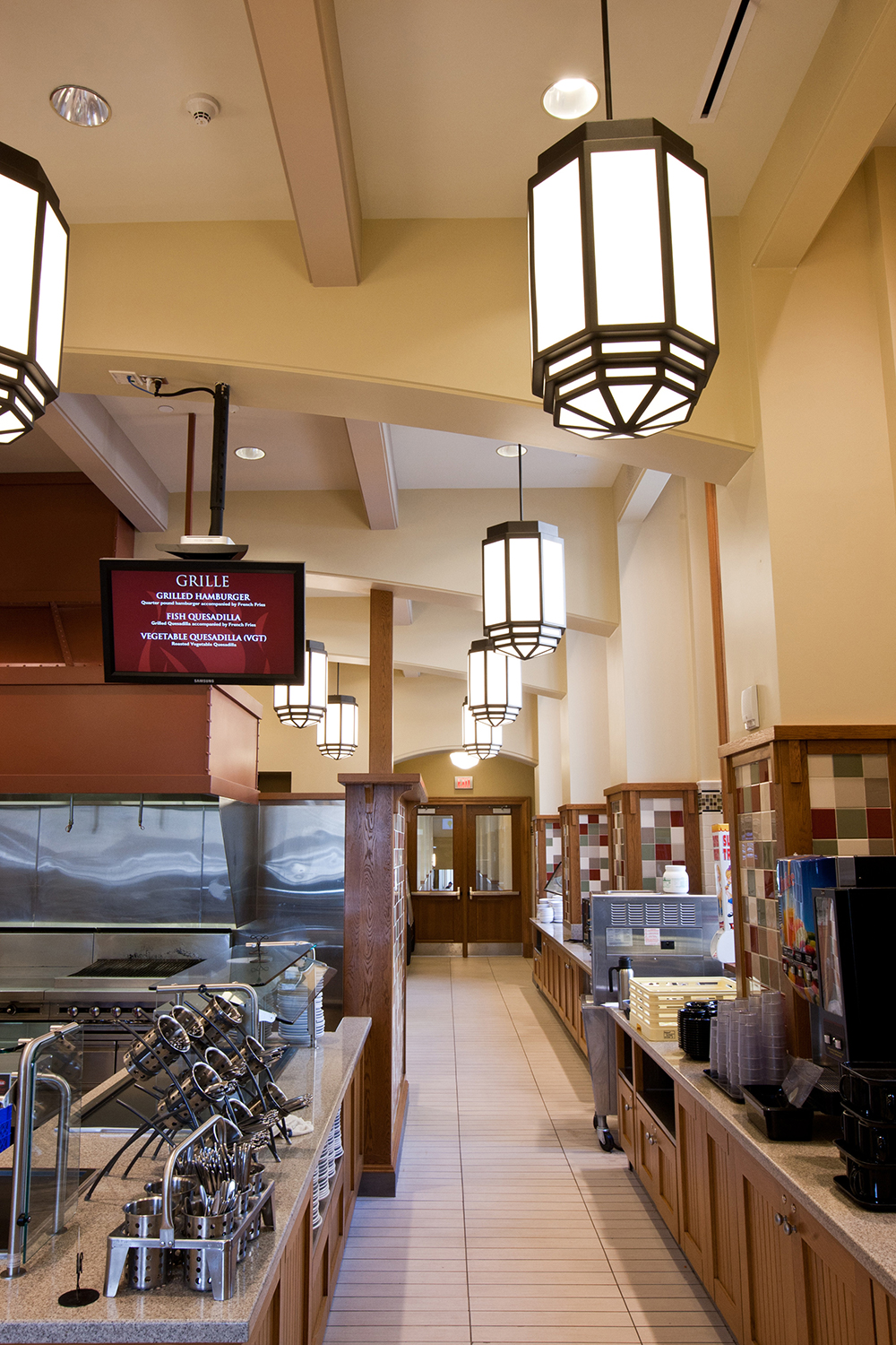 Bold, lantern-style custom light fixtures lined above a clean, classically styled campus kitchen.