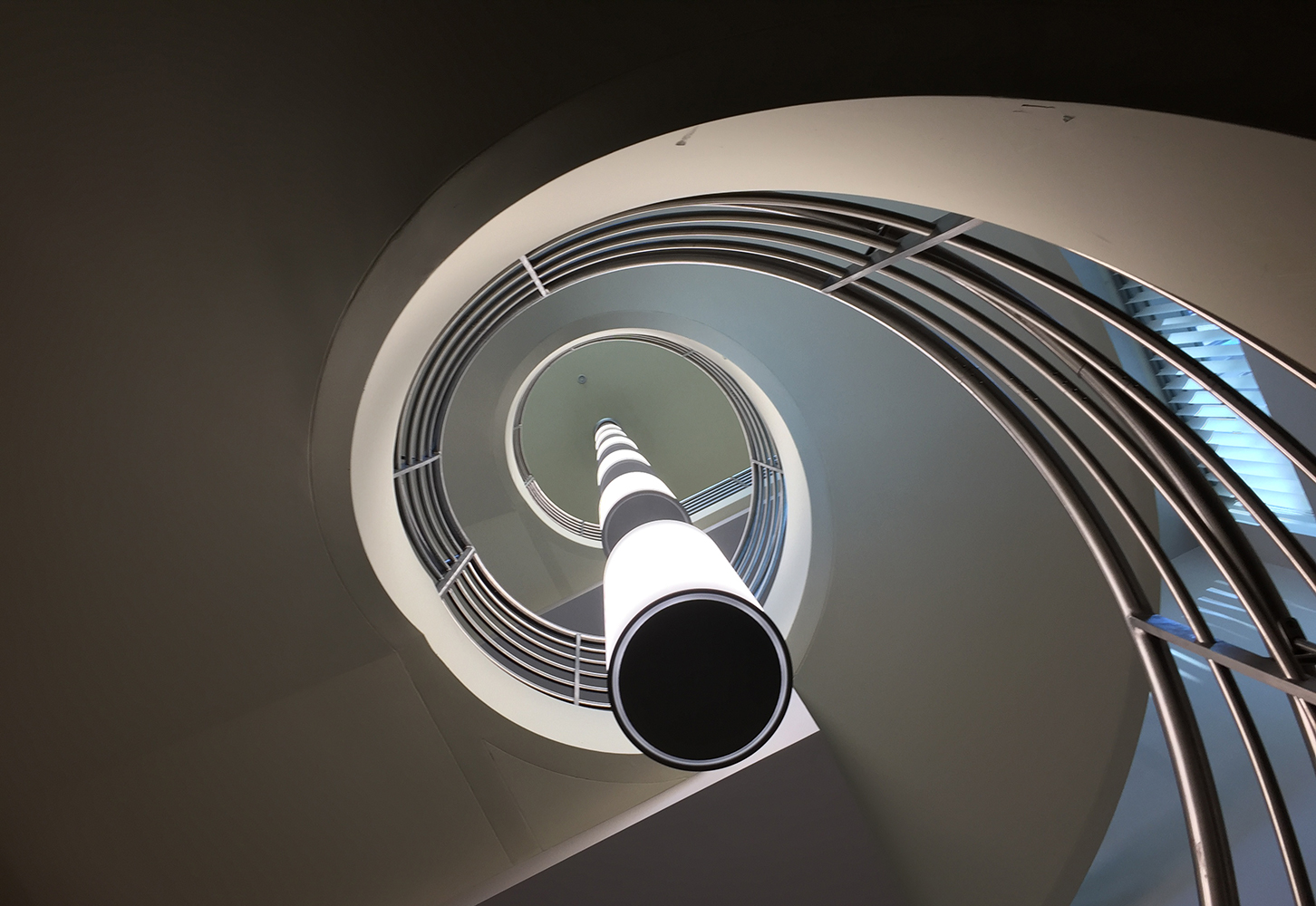 These clean, cylindrical custom light fixtures are hung in tandem down the center of round office stairwell