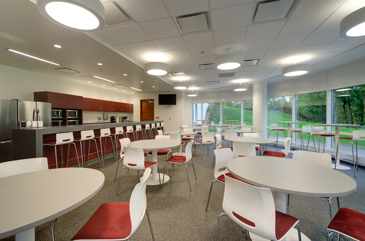 Omnience office lighting fixtures in a workplace cafeteria with round tables and large windows.