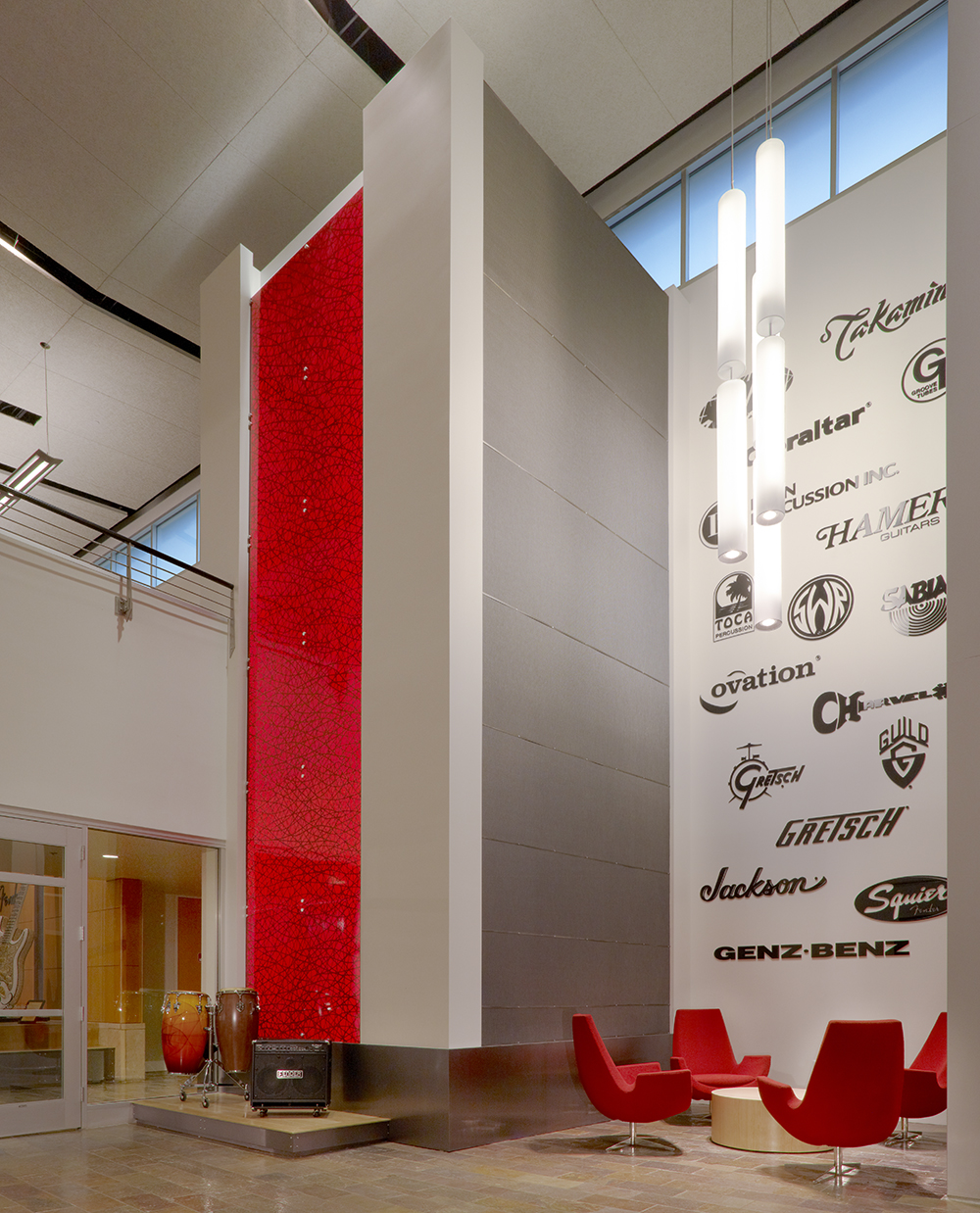Sequence pendants provide eye-catching illumination in a large light fixture configuration for a high-ceiling lobby above red chairs.