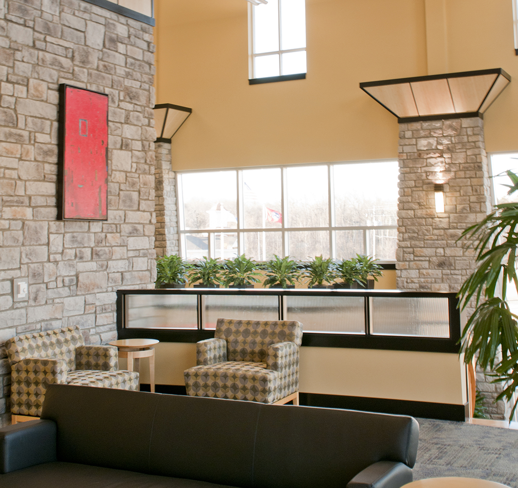 Wedge custom sconces illuminate commercial and office lighting designs, seen here on a stone wall in a seating area.