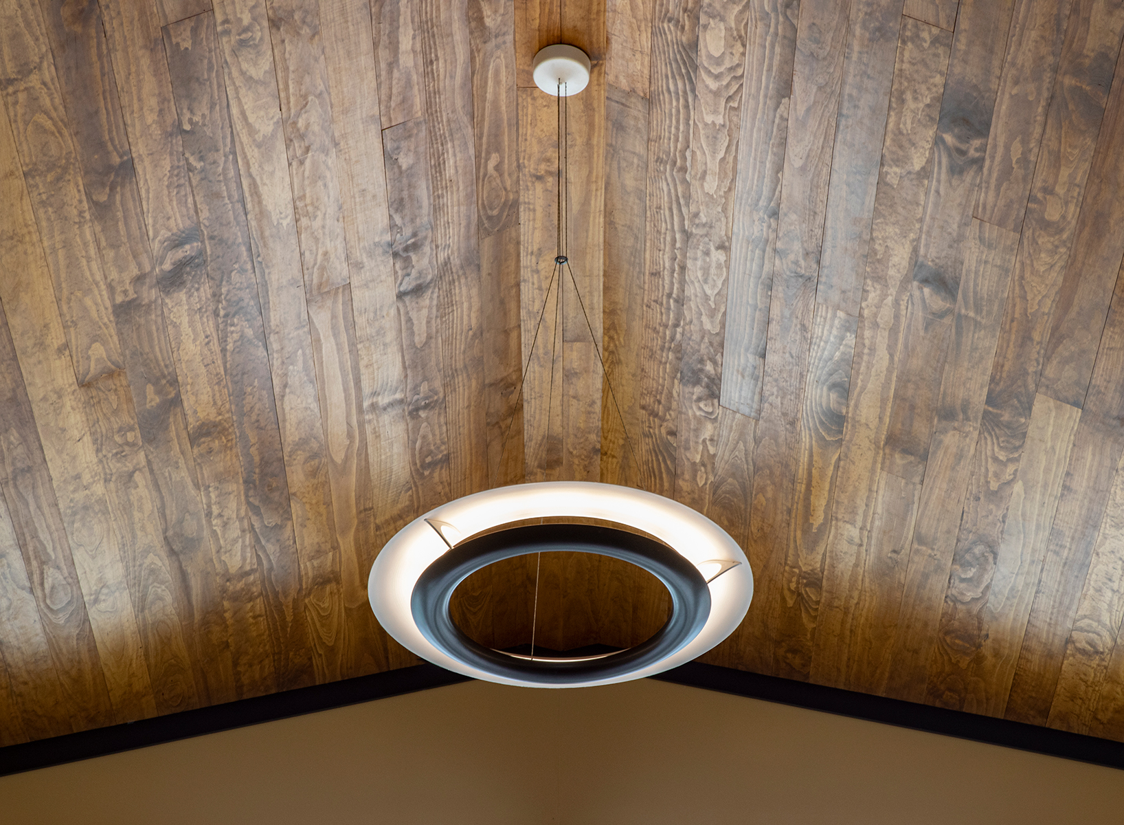 Cosmo ring pendant suspended below a natural wood cathedral ceiling