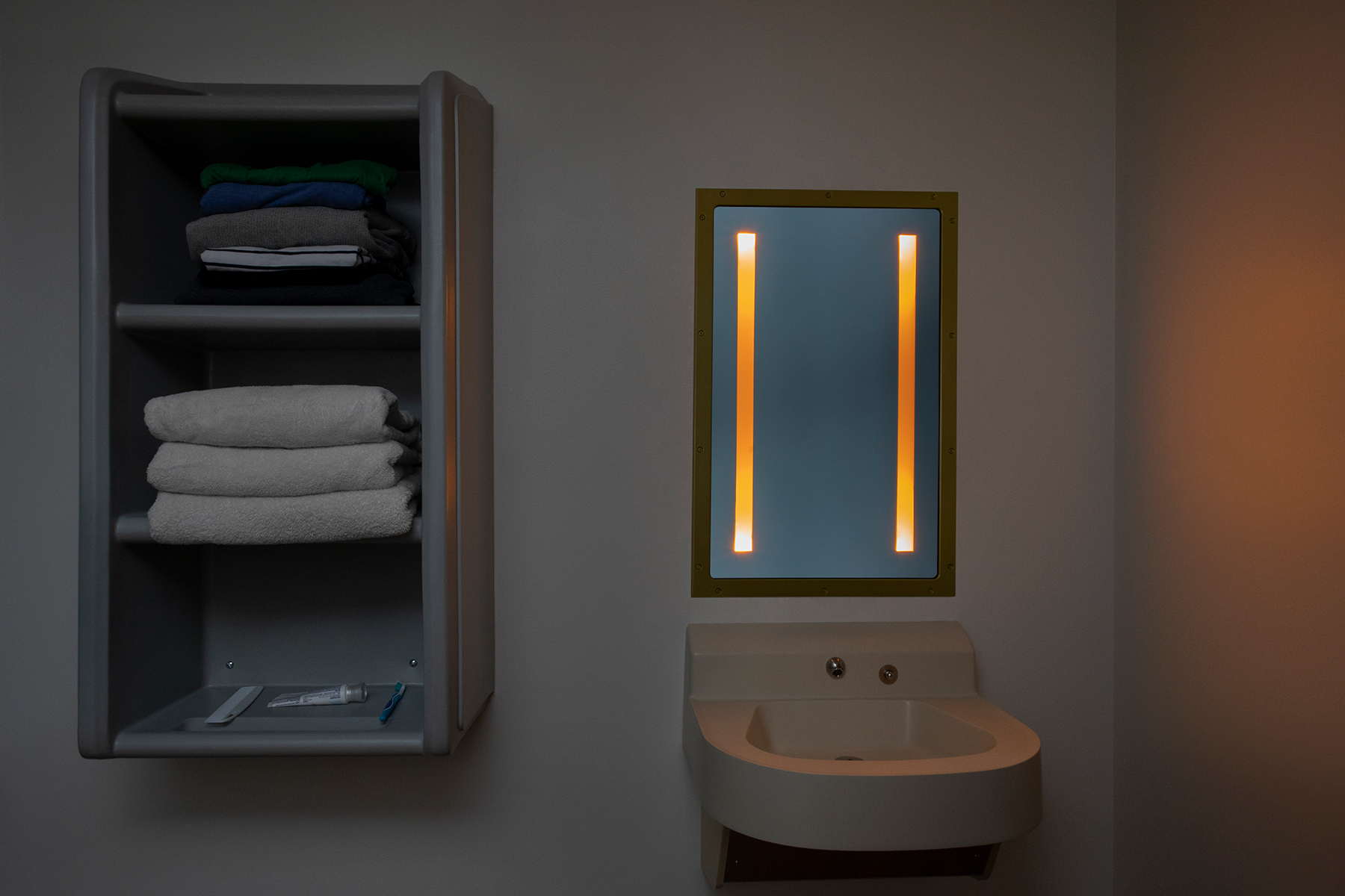 Sole rectangular illuminated mirror in a behavioral health bathroom with nightlight mode on